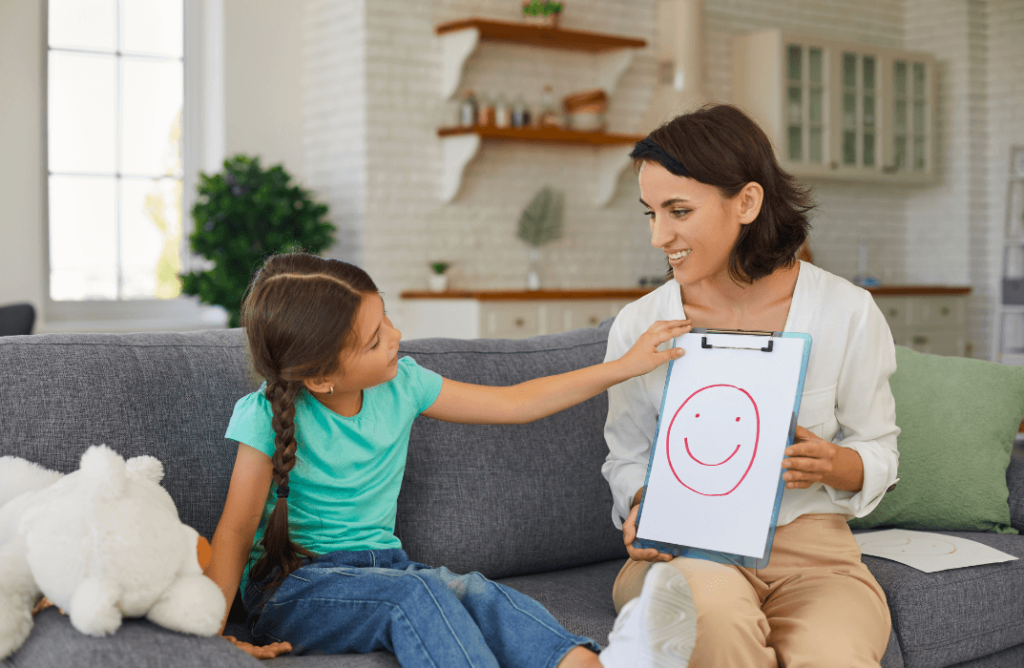 A young girl and therapist engage in ABA therapy at home, with a smiley face drawing, fostering a supportive and positive learning environment.