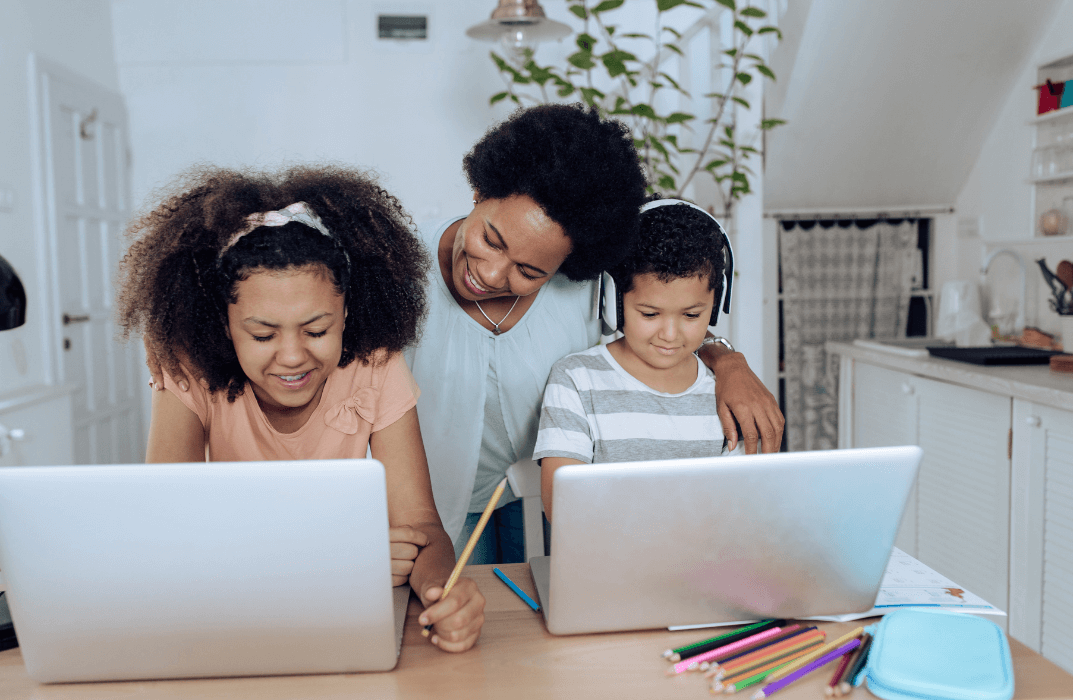 Mother supporting two children in home learning with laptops in a bright and organised home setting.